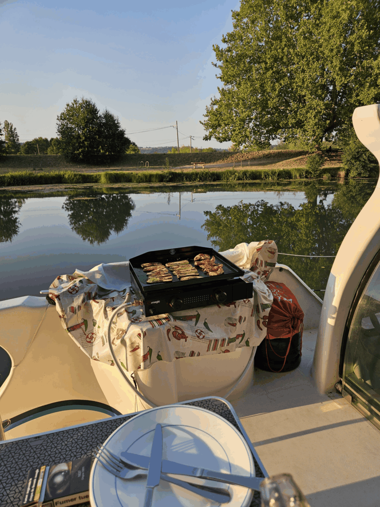 Plancha et table dressée à l'arrière du bateau SHIMA, au bord du canal au soleil couchant