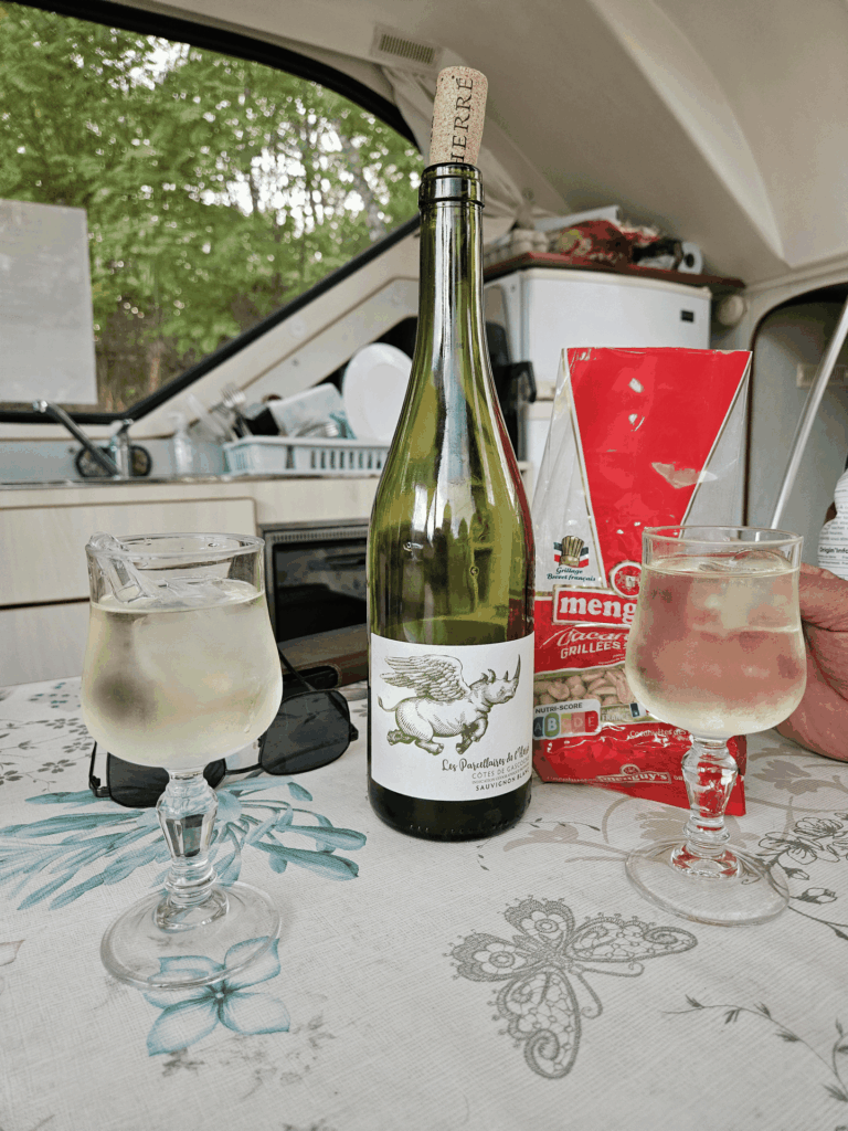 Bouteille de vin blanc des Côtes de Gascogne, deux verres et des cacahuètes sur la table du carré du bateau SHIMA