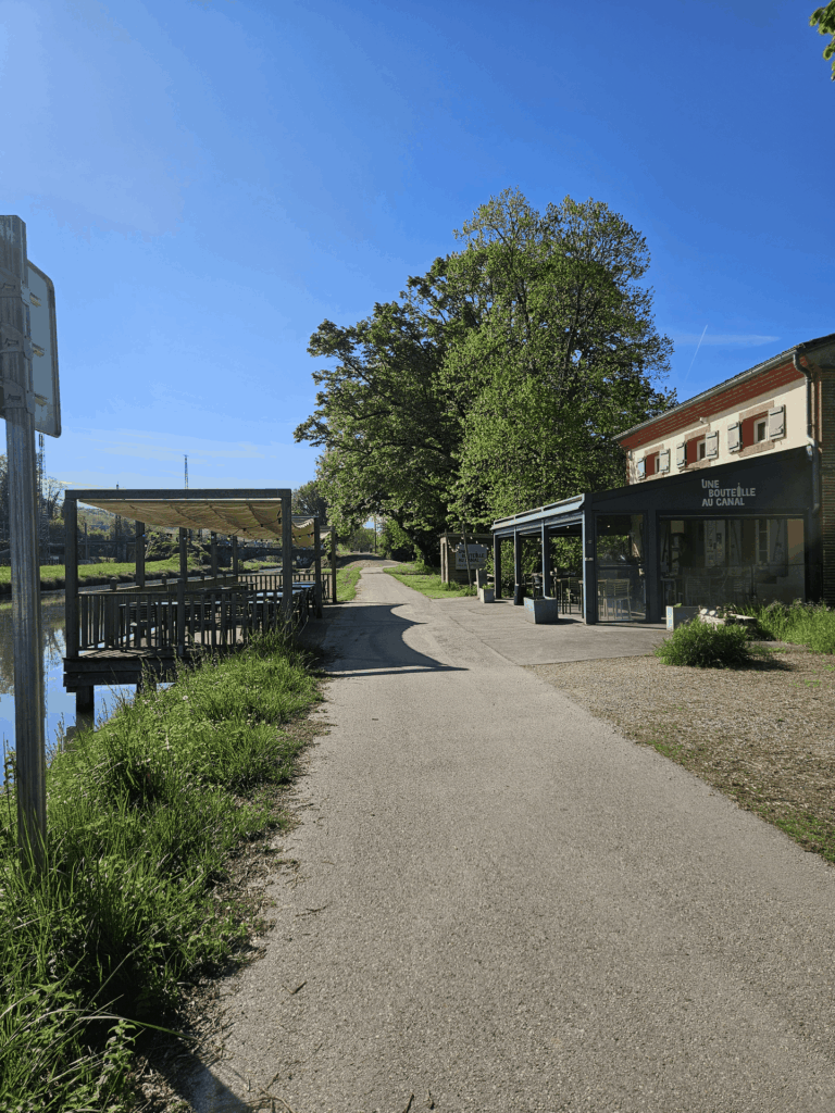 Chemin de halage le long du canal, bordé d'arbres, avec la terrasse d'un restaurant au bord de l'eau