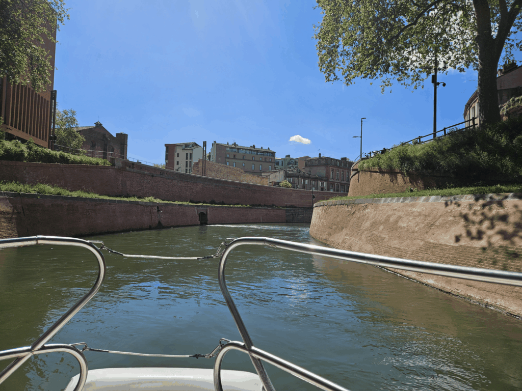 Depuis l'avant du bateau, navigation entre les hauts murs de brique d'un canal en ville