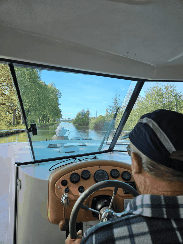 Un homme à la barre depuis le poste de pilotage intérieur du SHIMA, une passagère à l'avant, un pont droit devant