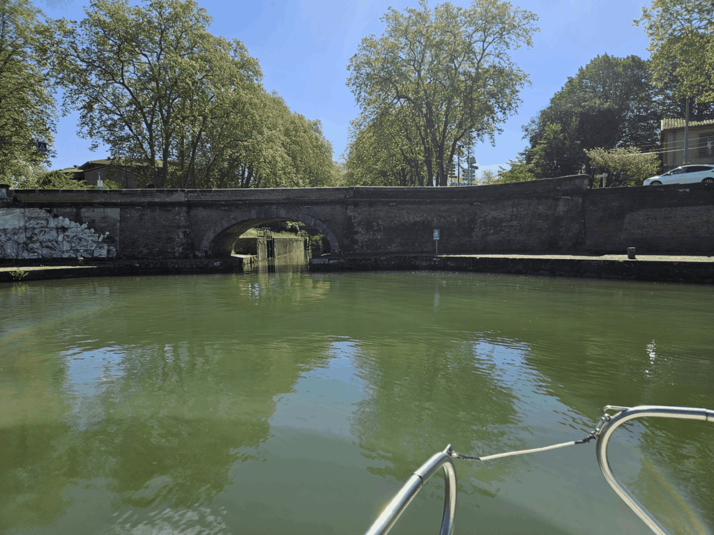 Depuis l'avant du bateau, un pont de brique en arche avec une écluse visible dans l'ouverture
