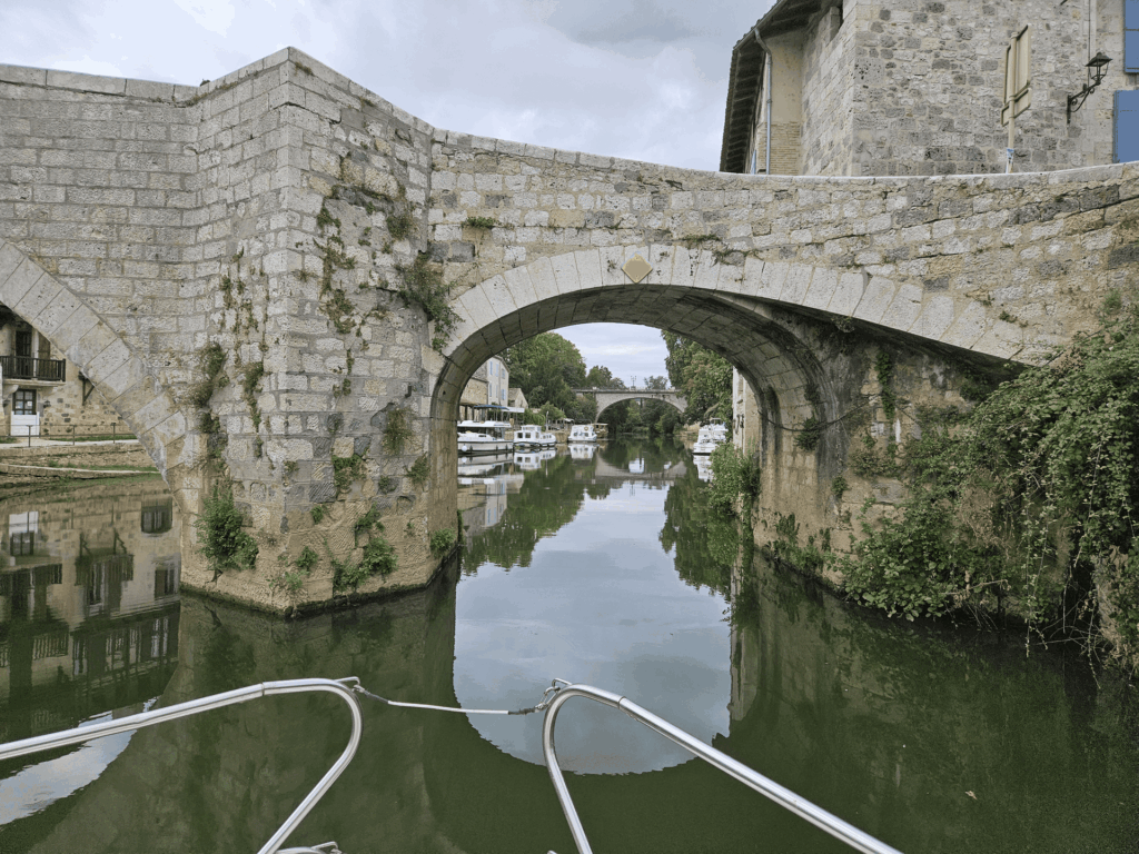 Un pont de pierre en arche au-dessus du canal, des bateaux amarrés et les maisons du village au-delà
