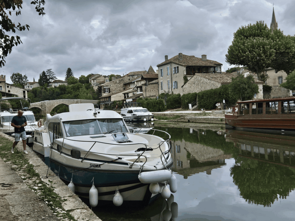 Le bateau SHIMA amarré au quai d'un village de pierre, devant un pont ancien et un clocher