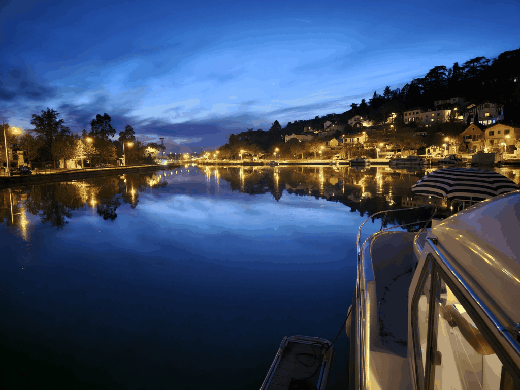 Le port à la tombée de la nuit vu depuis le pont du bateau, les lumières du village se reflétant dans l'eau